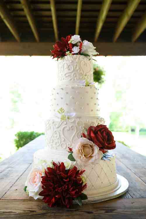 کیک خامه ای چهار طبقه سفید با تزئین گل برروی آن