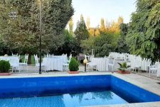 تصویر بند انگشتی نمایی از استخر روباز باغ تالار سپید ورامین در کنار فضای سبز و معماری روستیک مجموعه